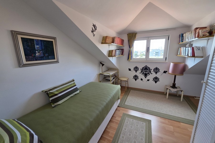 Ljust vindsrum med enkelsäng, arbetsplats och snedtak