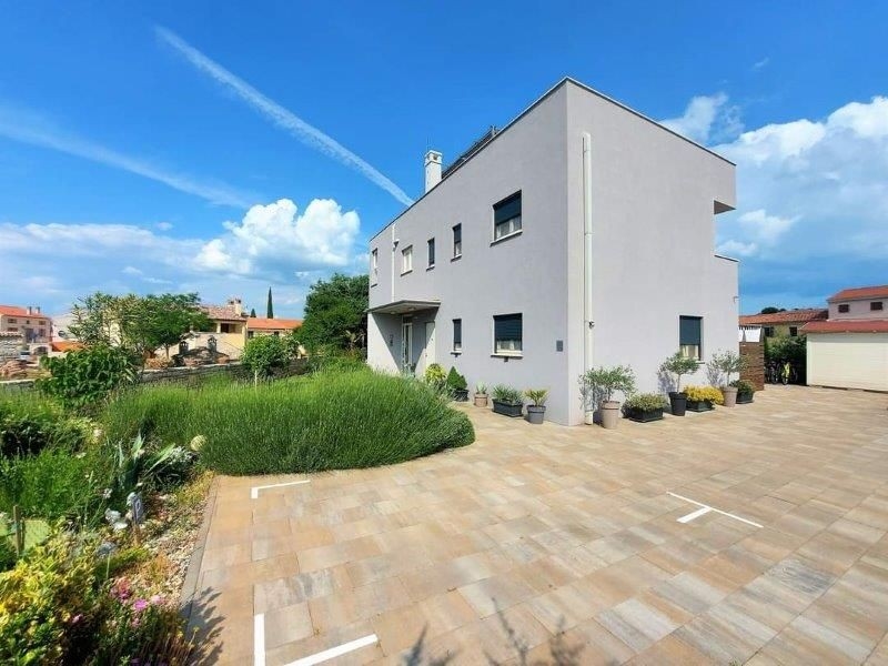 Framifrån av ett modernt hus med tre lägenheter till salu i Istrien, med en stenlagd förgård och omgiven av krukväxter.