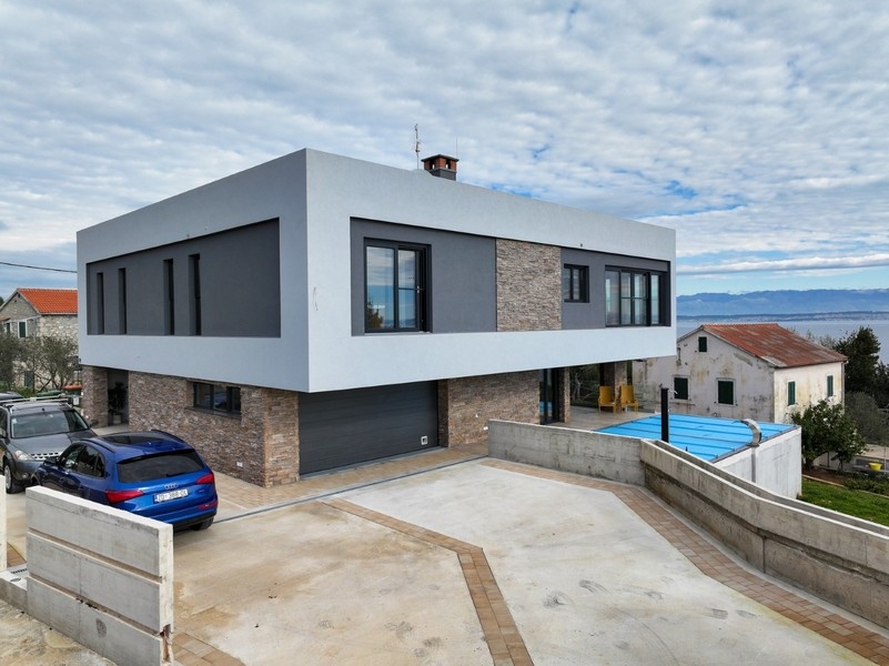 Framifrån av en modern villa med garage till salu på Ugljan i Kroatien, omgiven av en asfalterad uppfart och delvis havsutsikt