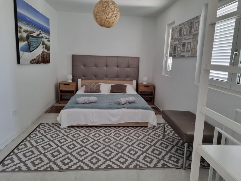 Sovrum i ett hyreshus i första raden mot havet, till salu i Karlobag, Kroatien, med en stor dubbelsäng, sängbord och en målning av en båt på havet.