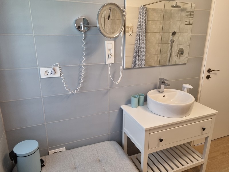 Badrum i lägenhetshus vid havet till salu i Karlobag, Kroatien, med ljusblått kakel, vit sminkkonsol, spegel och handdukstork