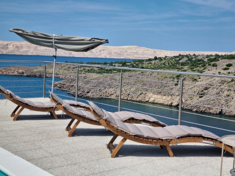 Relaxavdelning med solstolar och parasoll på terrassen i ett hyreshus i Karlobag, Kroatien, med havsutsikt.