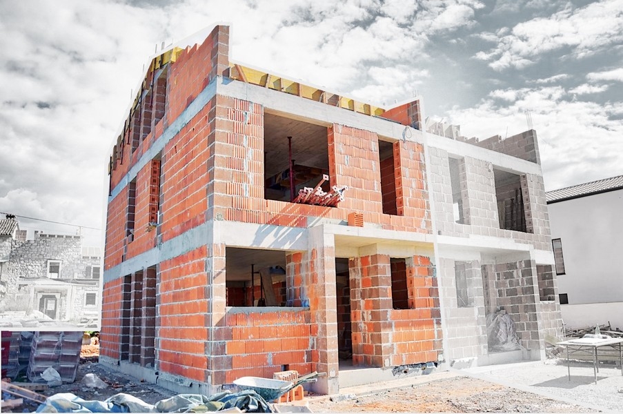 Halvfärdigt parhus i byggskede med synliga tegelväggar och öppningar för fönster och dörrar