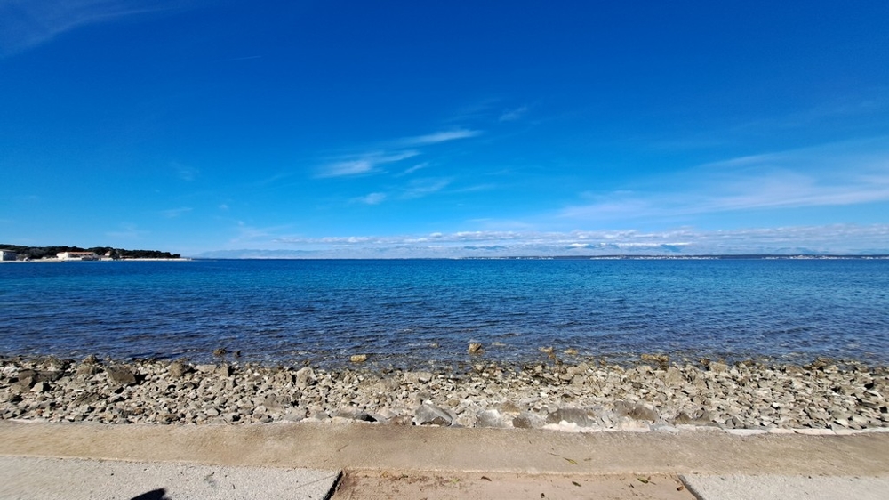 Pebble beach och klart hav framför en strandfastighet i Kroatien
