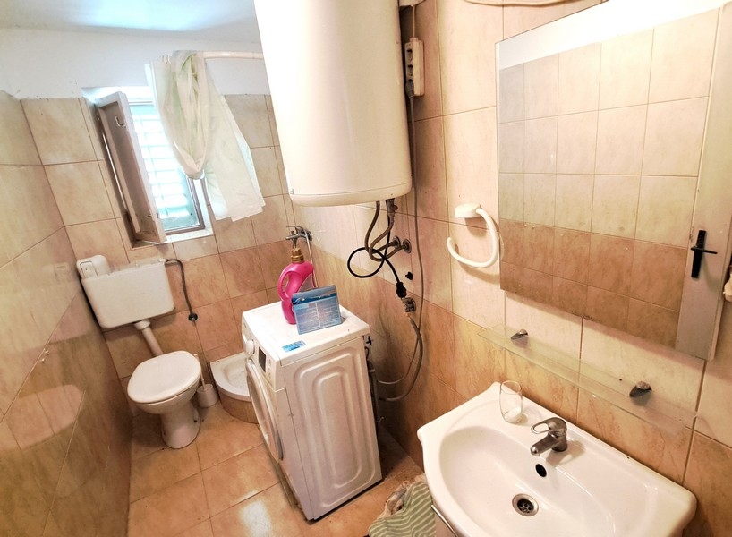 Badrum med beige kakel, standardtoalett, handfat och tvättmaskin i ett hus på ön Pasman i Kroatien.