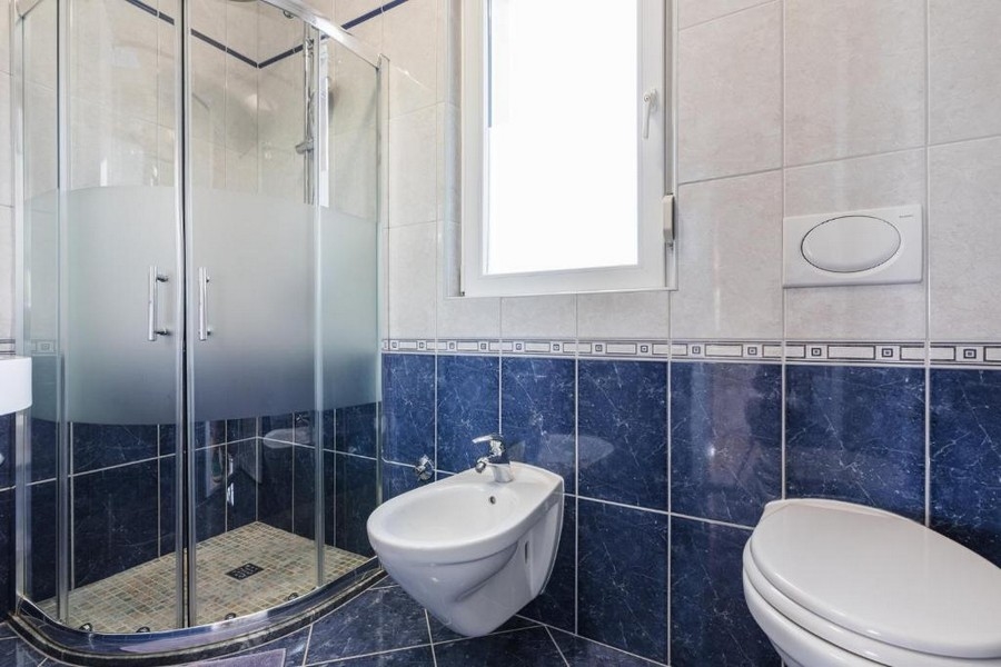 Badrum i en fastighet i Kroatien, hyreshus med havsutsikt, med hörndusch, bidé och toalett, ljusa väggar och mörkblått kakel