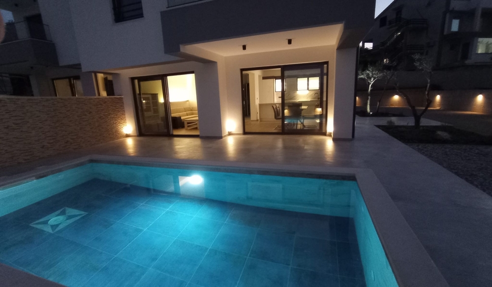 Skymningsvy över terrassen och poolen på en fastighet i Kroatien, invändig belysning skapar en välkomnande atmosfär.