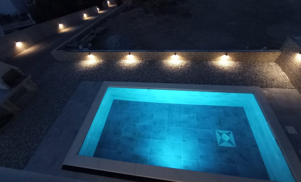 Nattvy av en pool med blå belysning och delvis skymd utsikt över fastigheten i Kroatien i bakgrunden.