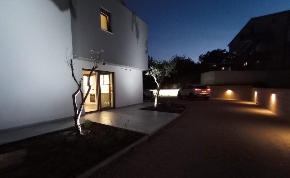 Nattbild av en fastighet i Kroatien med exteriörbelysning och en bil parkerad på gården.