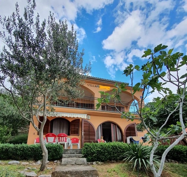 Exteriör vy av en tvåvåningsvilla med en orange fasad och välvda fönster omgivna av träd och grönområden