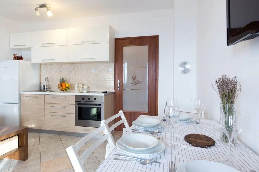 Modernt kök och matplats med vita och träskåp, ett dukat matbord och utsikt över vardagsrummet.