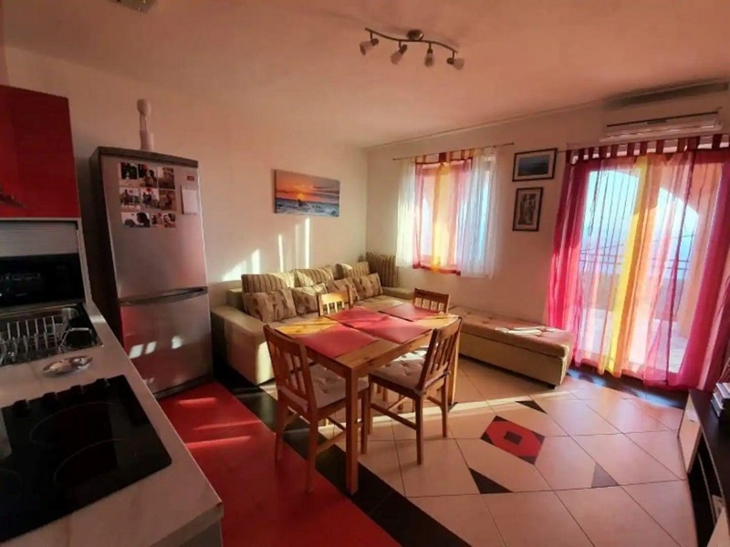 Soligt vardagsrum och matplats med röda och gula accenter, utrustad med matbord, soffa och tillgång till balkongen.