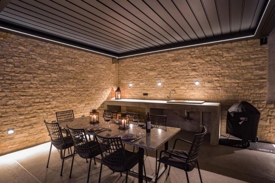 Täckt uteområde med matplats och grill, omgiven av stenmurar