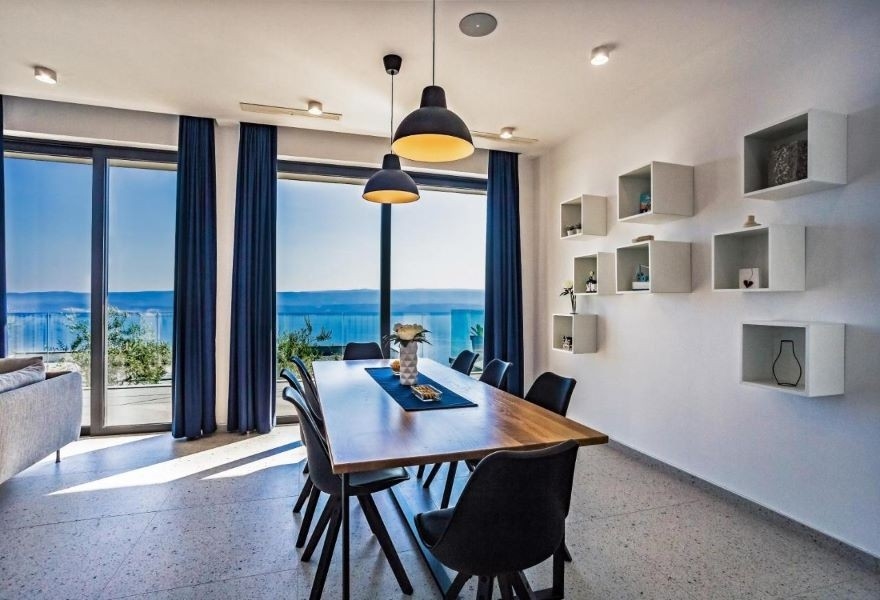 Matsal med modernt träbord, svarta stolar och panoramautsikt över havet