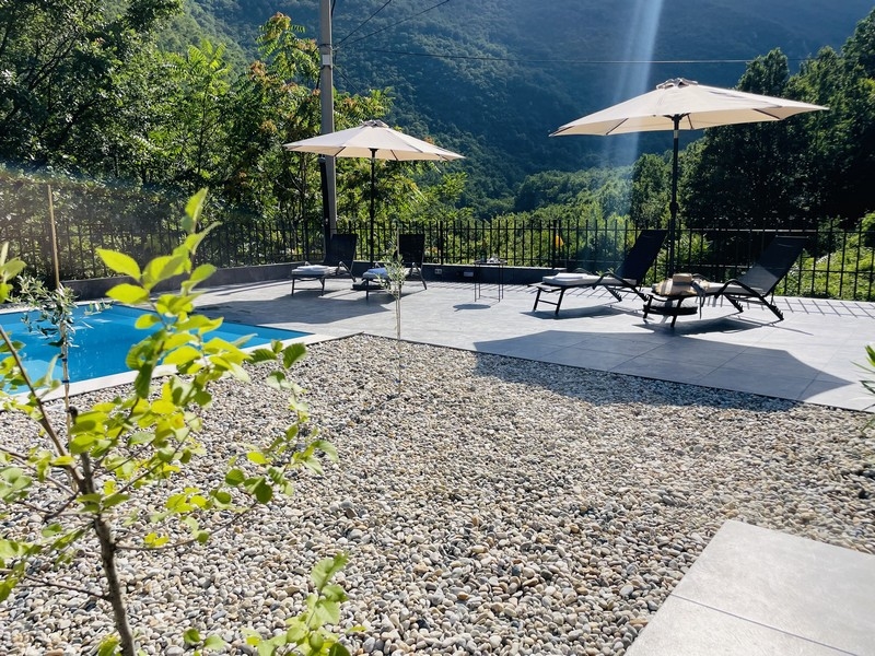 Solterrass vid poolen med solstolar och parasoll, omgiven av grön natur