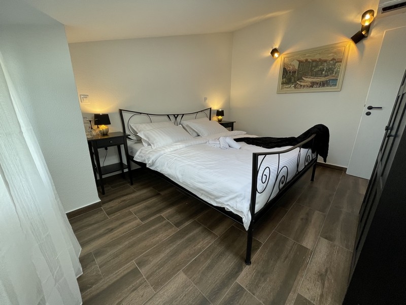 Sovrum med säng i smidesjärn, trägolv och vägglampor, med sidovy av en målning