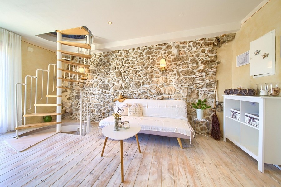 Mysigt vardagsrum med exponerade stenväggar, soffa och spiraltrappa som leder upp.