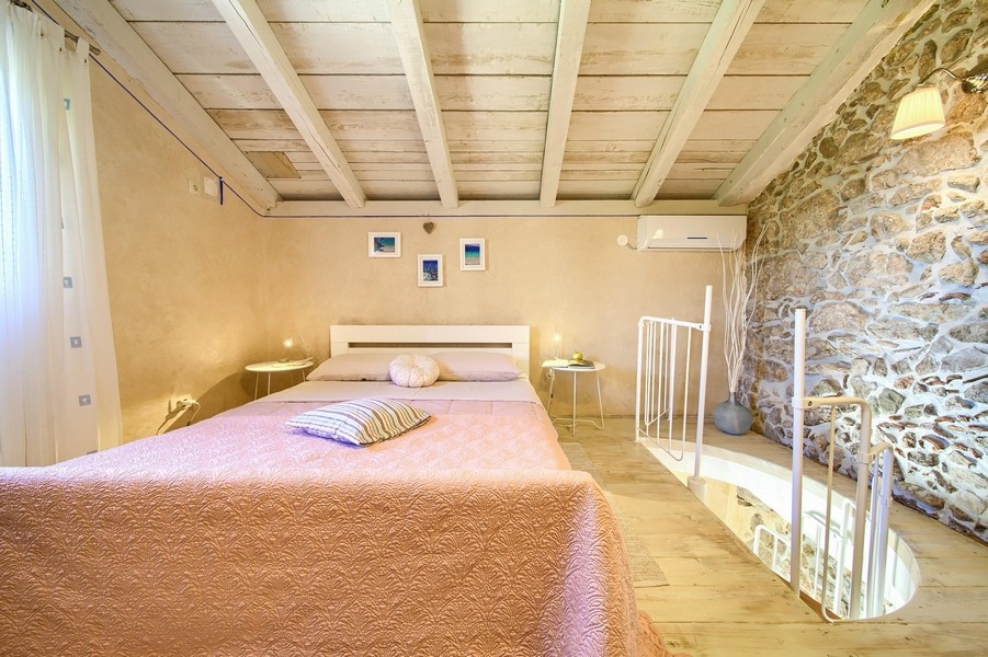 Sovrum med takbjälkar i trä och rustik inredning, nås via en spiraltrappa.