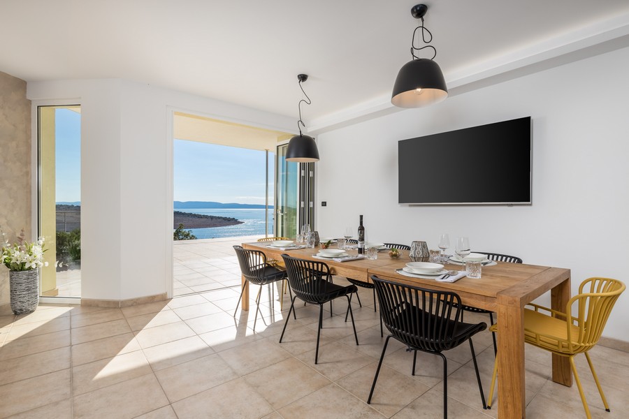 Matplats med stort träbord, moderna stolar och direkt tillgång till terrassen med havsutsikt.