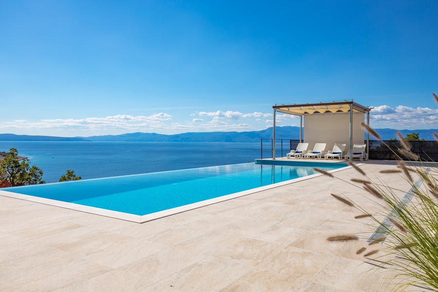 Infinitypool med solstolar, direkt havsutsikt och blå himmel.