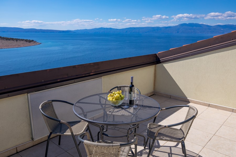 Terrass med bord och stolar, utsikt över havet och de omgivande kullarna i bakgrunden.