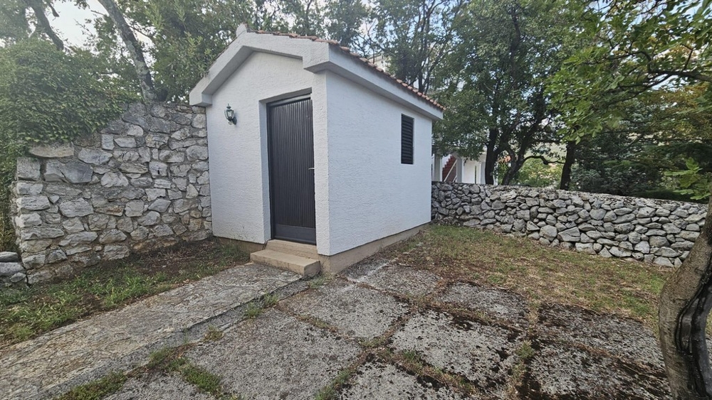 Litet uthus i trädgården med stenmur