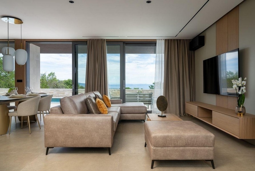 Vardagsrum med stora glasfönster och utsikt över poolen