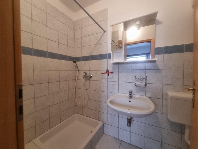 Ljust badrum med klinker, dusch och enkelt handfat.