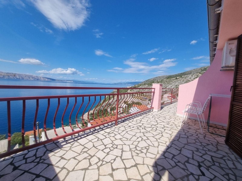 Stor öppen terrass med mosaikstensgolv, röda räcken och utsikt över havet och den omgivande landsbygden.