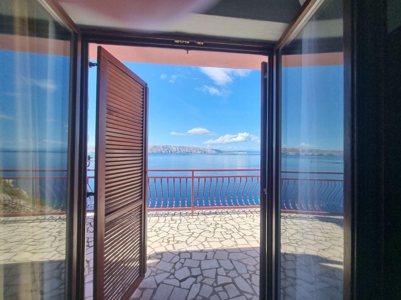 Utsikt från ett rum genom en öppen dörr mot en terrass med havsutsikt.