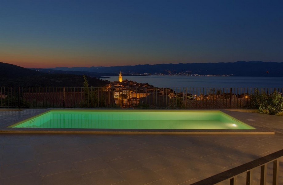 Upplyst pool på natten och utsikt över Vrbnik i Kroatien.