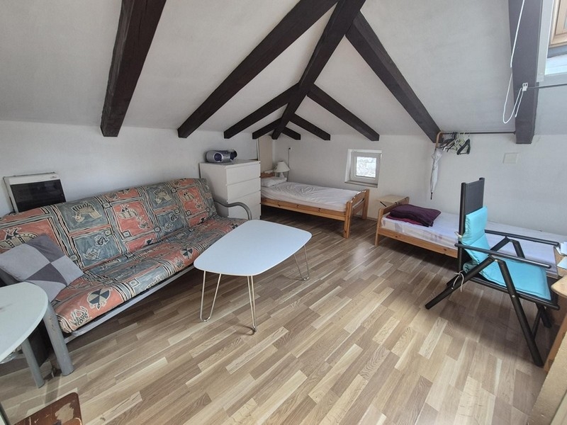 Öppen planlösning på vinden med två sängar och träbjälkar i taket.