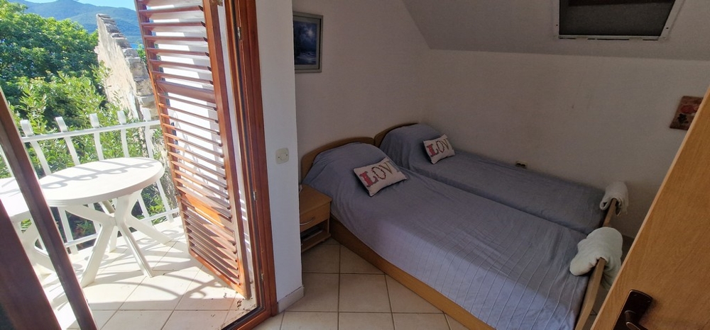 Ett sovrum med två enkelsängar täckta med blå filtar. Det finns en liten balkong med runt bord och stolar och utsikt över grönskan.