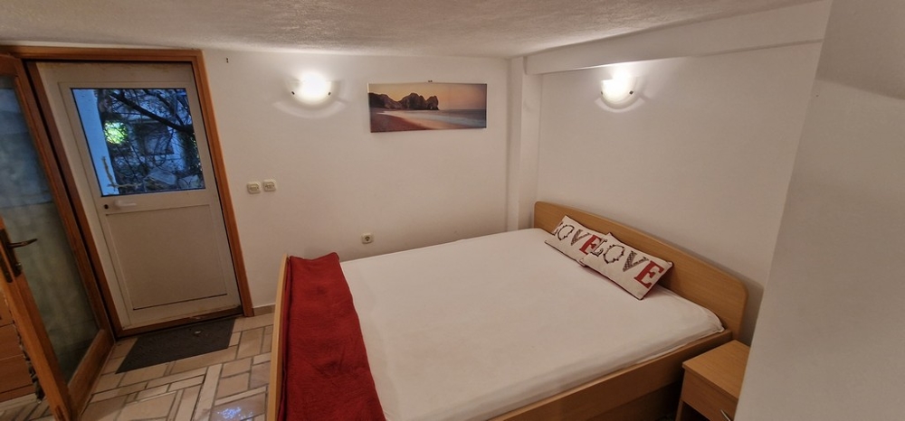 Ett sovrum med en dubbelsäng dekorerad med vita och röda accenter. Det finns en bild av en strand på väggen och en dörr som leder utanför.