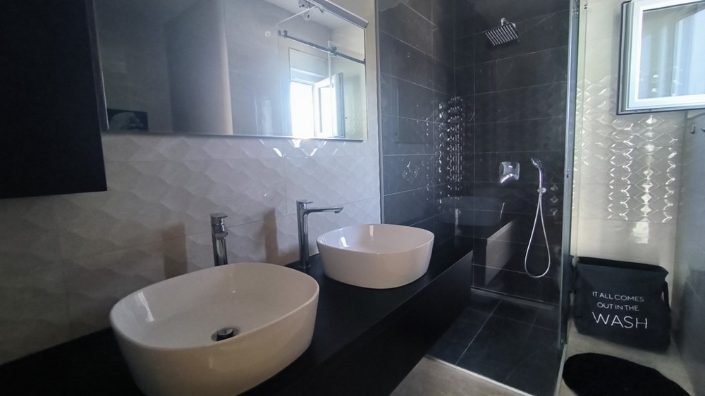 Modernt badrum med dubbla handfat och regndusch.