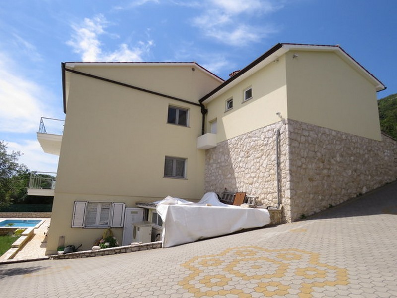 Exteriör vy av huset med asfalterad parkeringsplats och pool i bakgrunden.