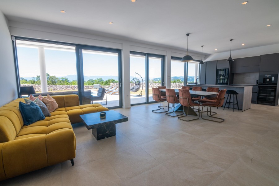 Vardagsrum med gul soffa, matplats och öppet kök, panoramafönster