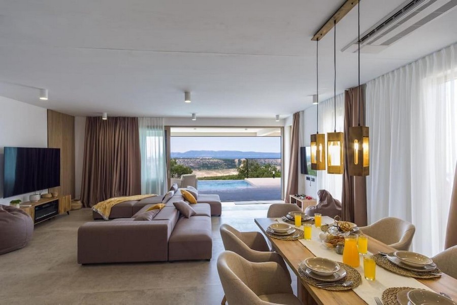 Modernt och lyxigt inrett vardagsrum med matplats och utsikt över poolen.