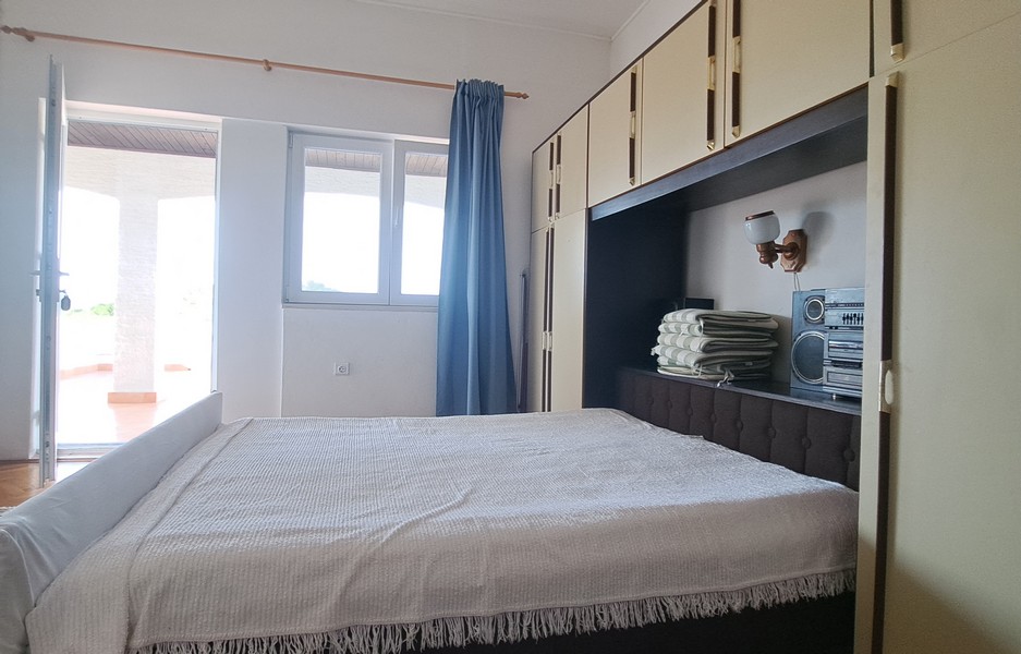 Sovrum med säng och inbyggt förvaringsutrymme, utsikt över uteserveringen.