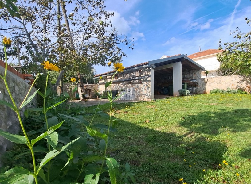 Uteplats med gräsmatta, träd och en stenstruktur.