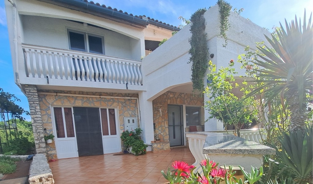 Framifrån av huset med balkong och trädgård.