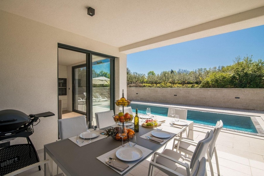 Täckt terrass med matbord och utsikt över poolen