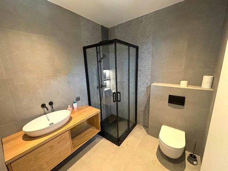 Modernt badrum med glasdusch och trähandfat