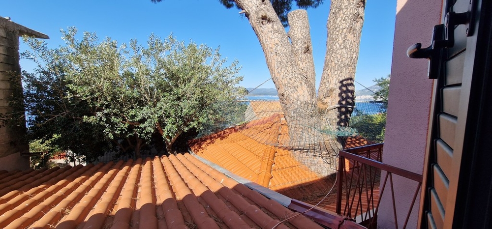 Utsikt från balkong över tegeltak, träd och hav