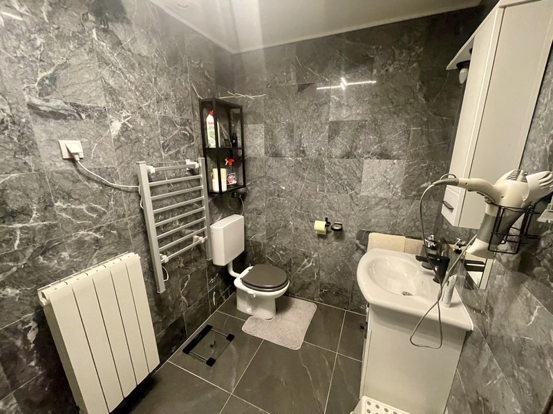 Modernt badrum med dusch, toalett och grått väggkakel