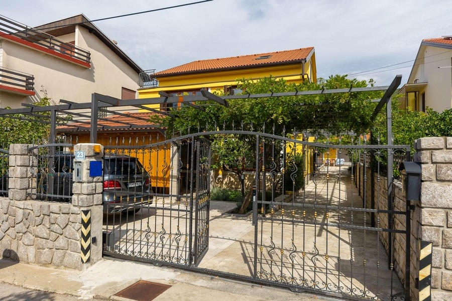 Fastighetsingång med grind och gult hus