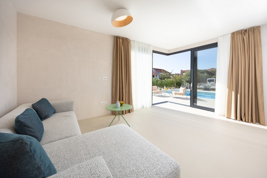 Vardagsrum med soffa och utsikt över terrassen och poolen