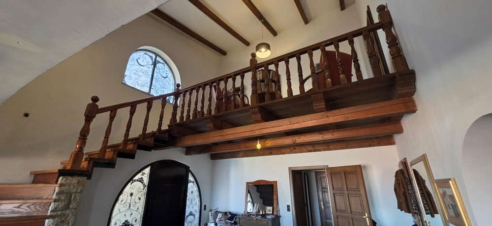 Vardagsrum med öppen spis, synliga träbjälkar och galleri