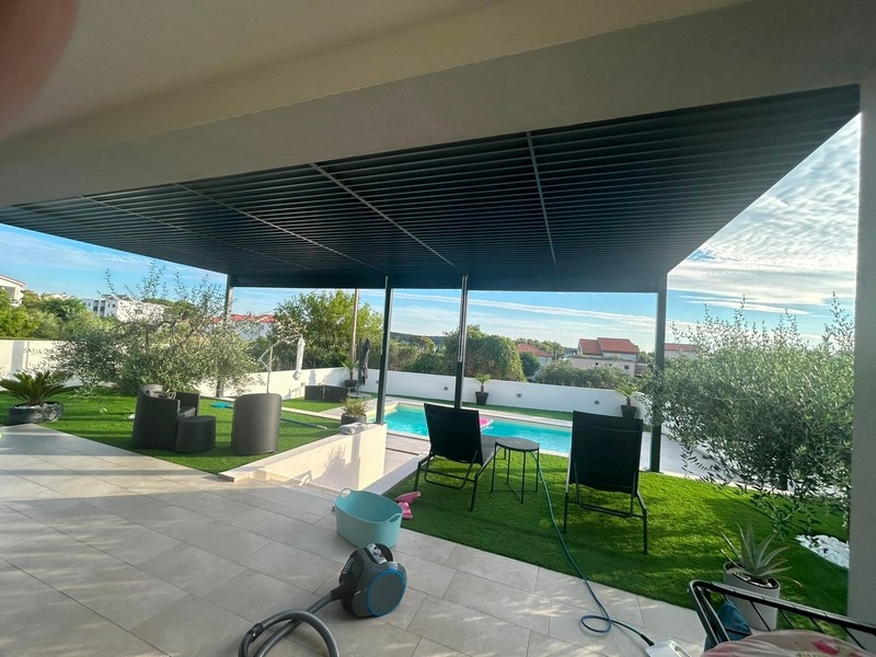 Täckt terrass med sittgrupp, gräsmatta och pool