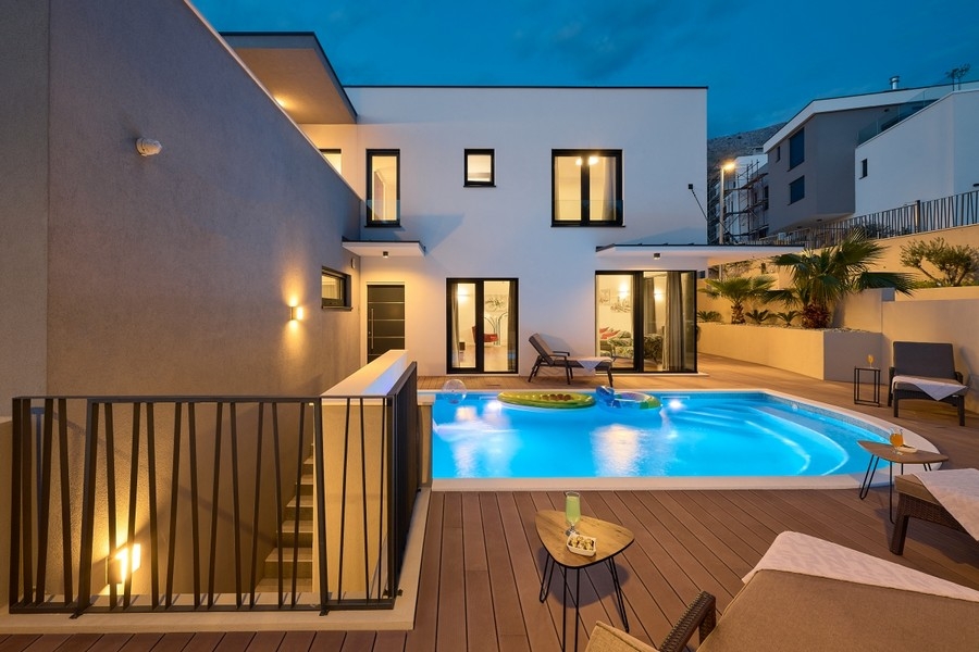 Poolområde med trädäck och upplyst villa